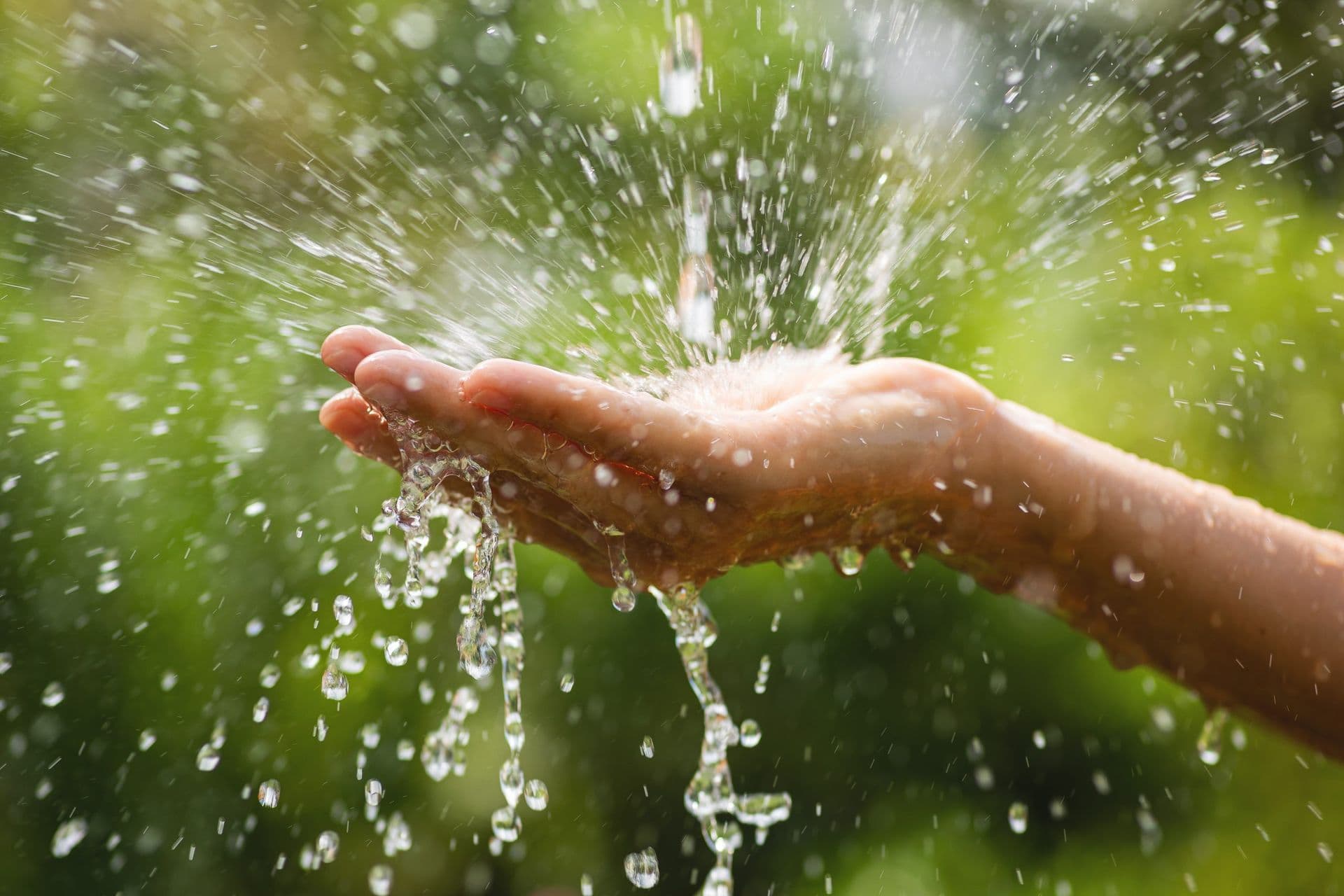 A close-up of an outstretched hand catching splashing water droplets, set against a blurred green background, conveying freshness and vitality.