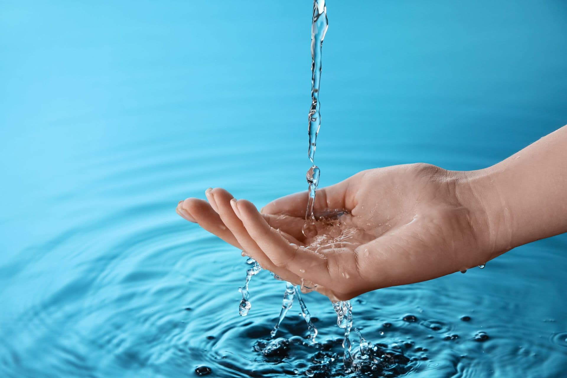 A hand catching flowing water over a calm, rippling blue surface, conveying a sense of tranquility and purity.