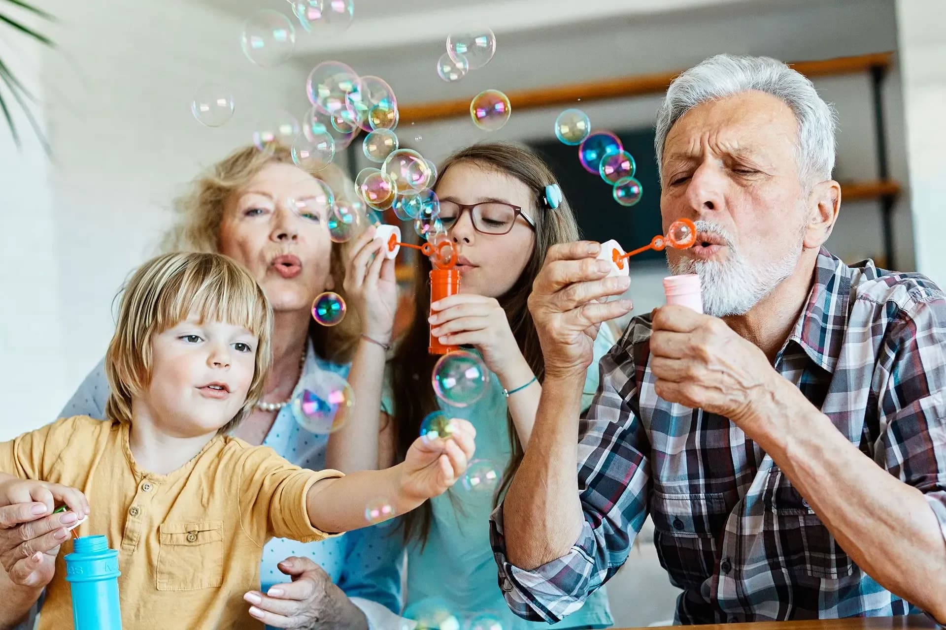 A joyful family scene with four people of different generations blowing colorful bubbles together. The atmosphere is playful and warm.