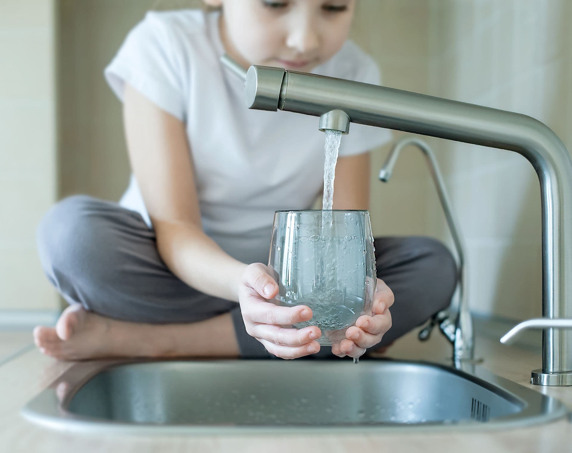 A young girl smiles while holding a clear glass of water in her hands.