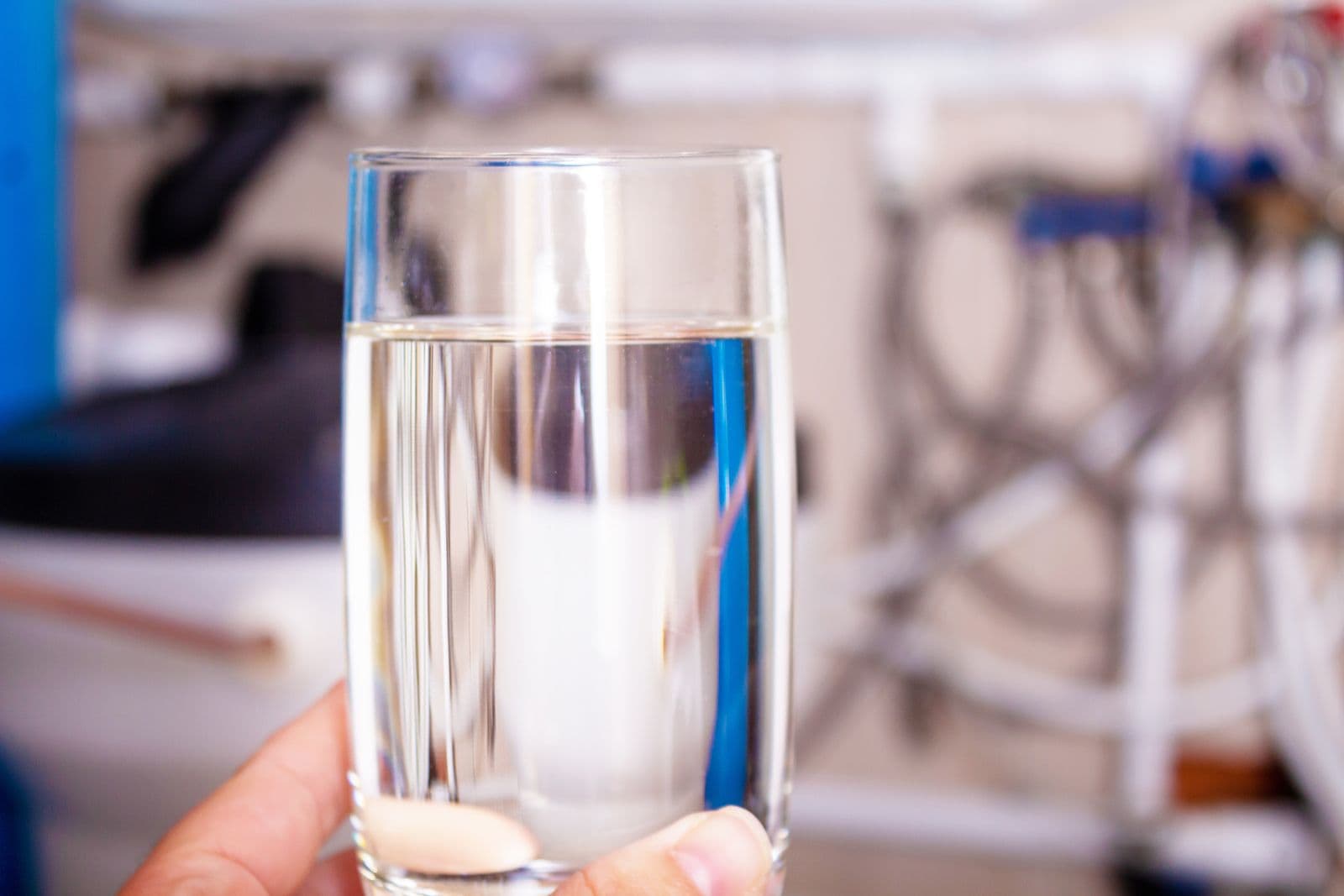Clean water glass in hand. Water softening. Home water filtration, softener and purification system in background. Health care concept.