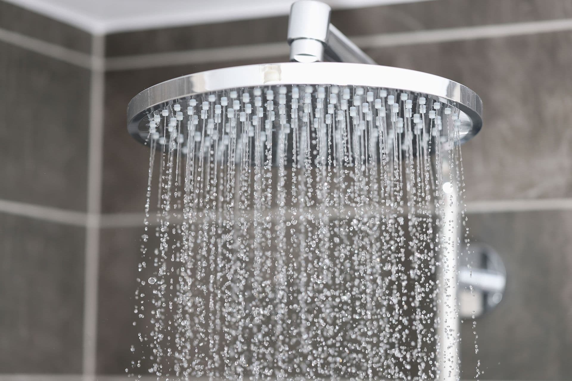 Showerhead spraying water in a tiled bathroom. The droplets glisten, creating a refreshing, invigorating atmosphere, highlighting modern design.