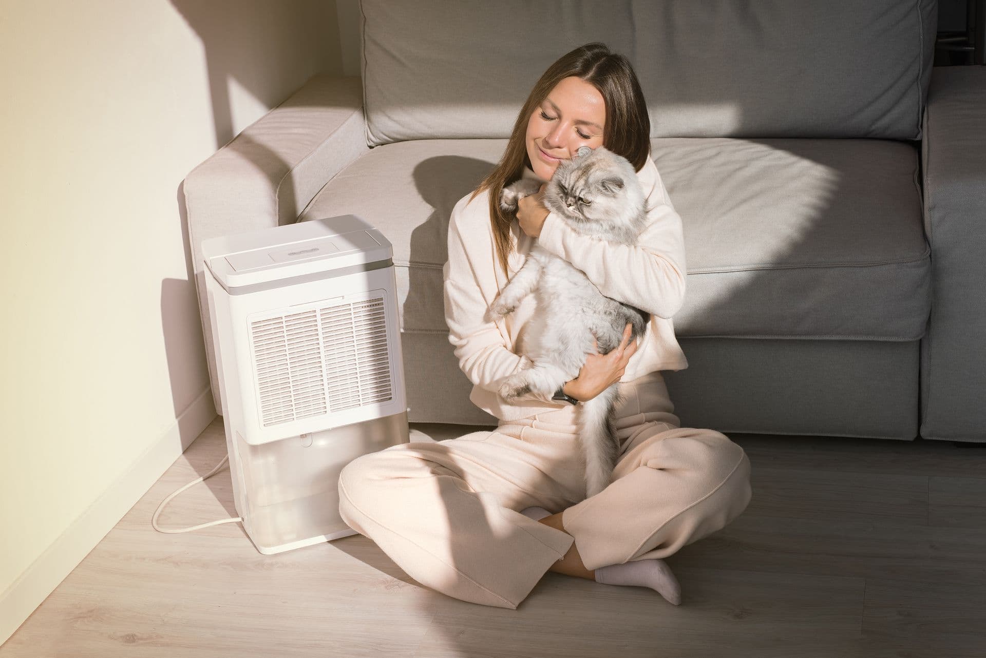 A woman sits on the floor, gently holding a small dog in her lap, both appearing relaxed and content.