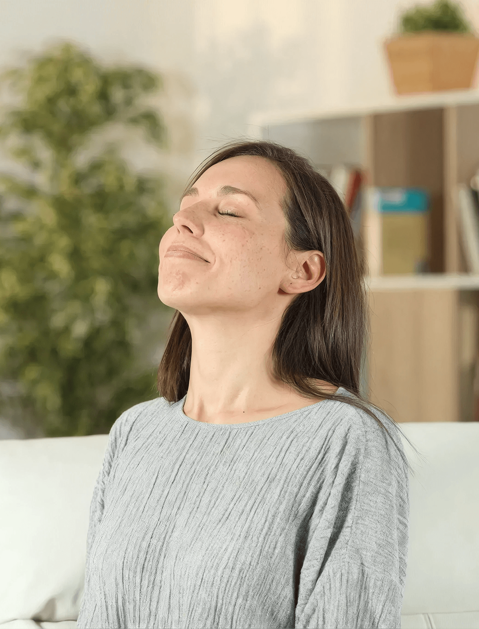 A woman sits on a couch, appearing relaxed as she breathes deeply, conveying a sense of calm and tranquility.